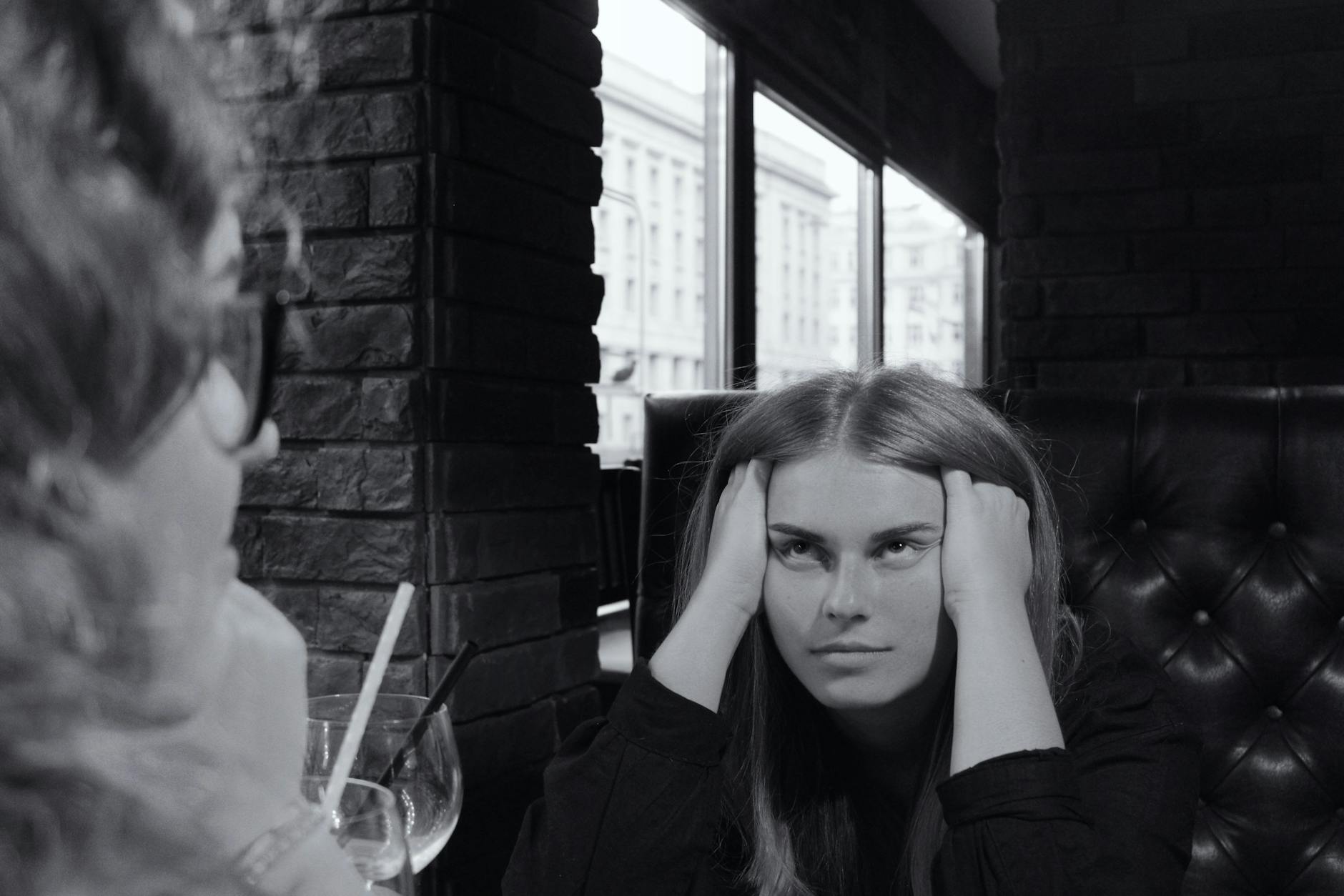 Monochrome photo of a pensive woman in a Warsaw cafe, capturing a moment of reflection.