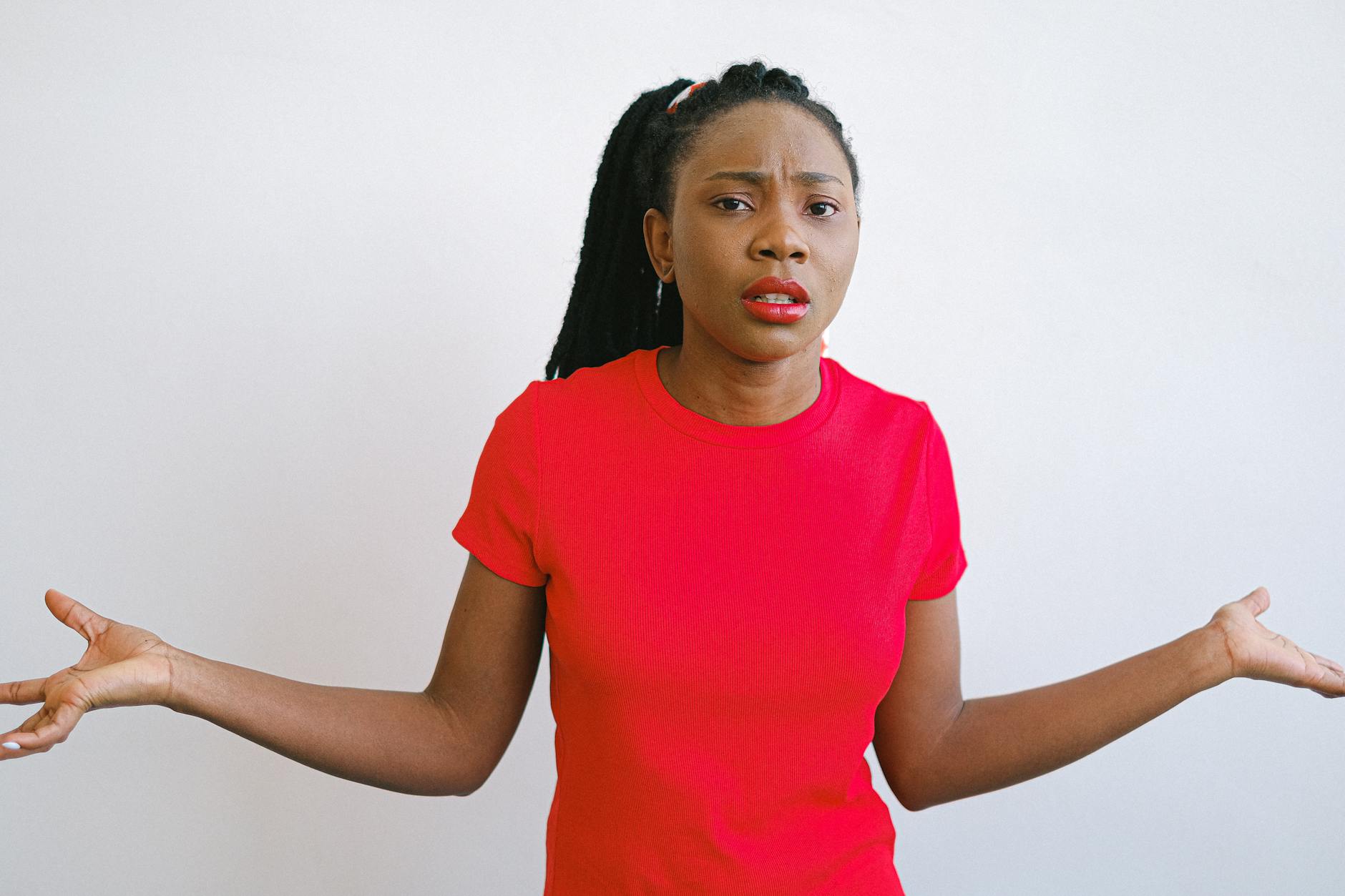 Young black woman in a red shirt with a confused expression. Perfect for emotive stock photo needs.