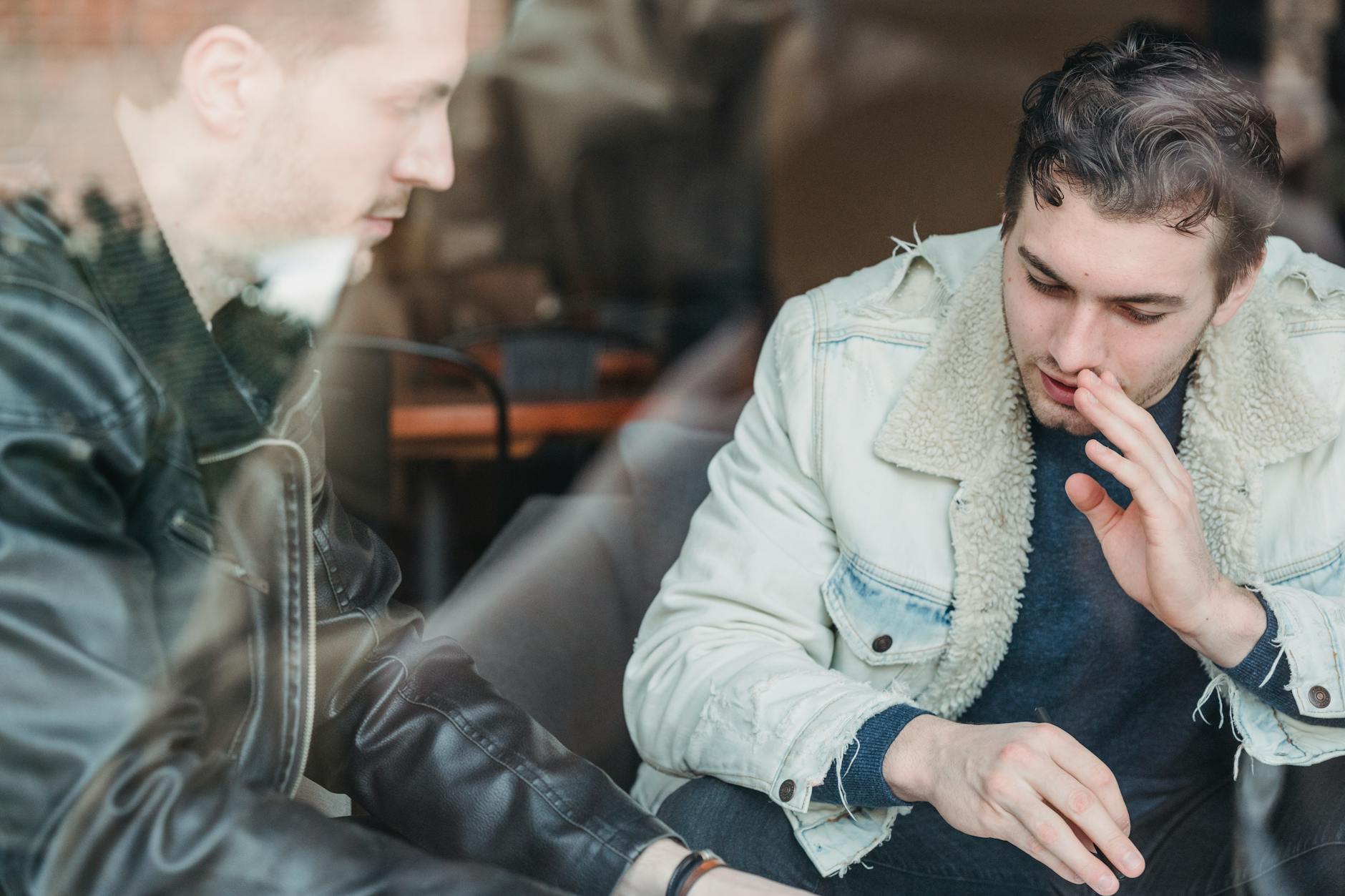 Two young men discussing business strategies in a cafe, seen through glass.
